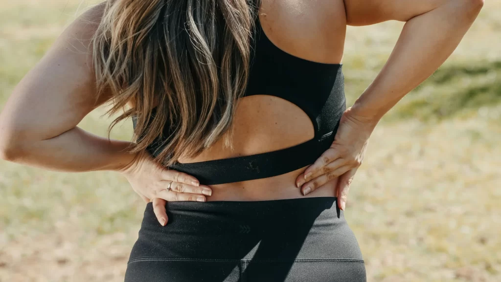 A woman in sports clothing touching her lower back in pain.